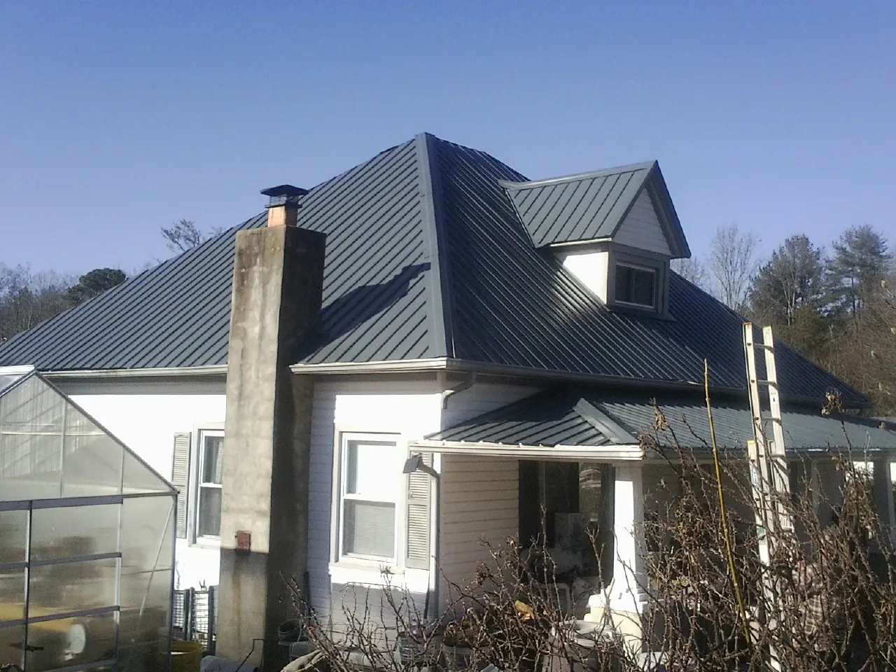 Dark blue standing seam metal roof on a white farmhouse with dormer — Slate & Tile Roof Repair by Roofing Brothers in Boys Town
