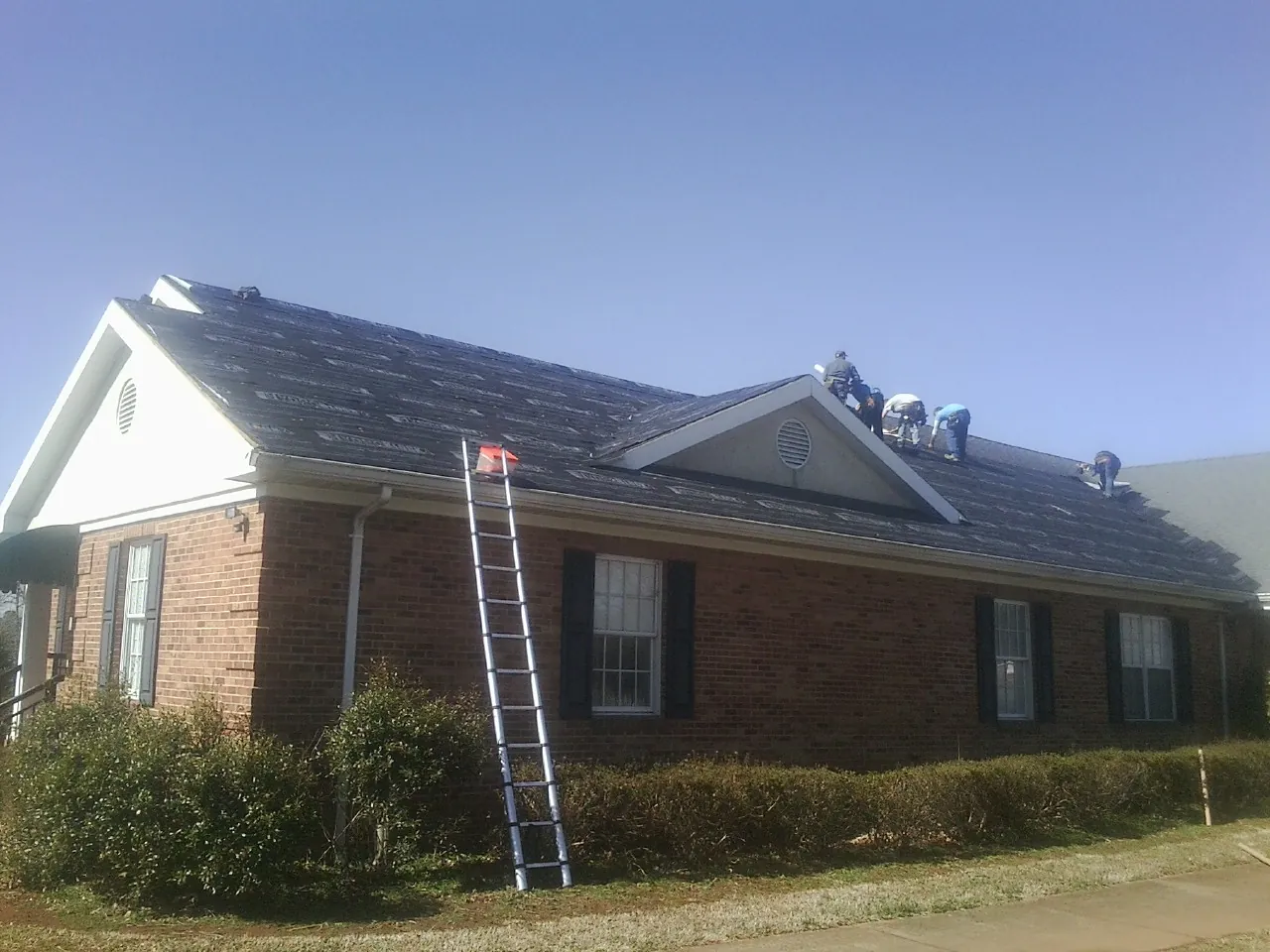 Crew tearing shingles off a brick ranch roof with a ladder set — Emergency Roof Repair work by our crew in Boys Town