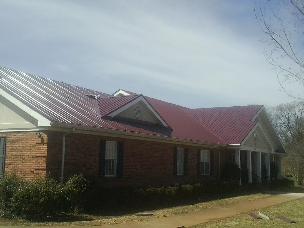 Red metal roof with gabled entries on a long brick building, from a Hail Damage Roof Repair job in Boys Town