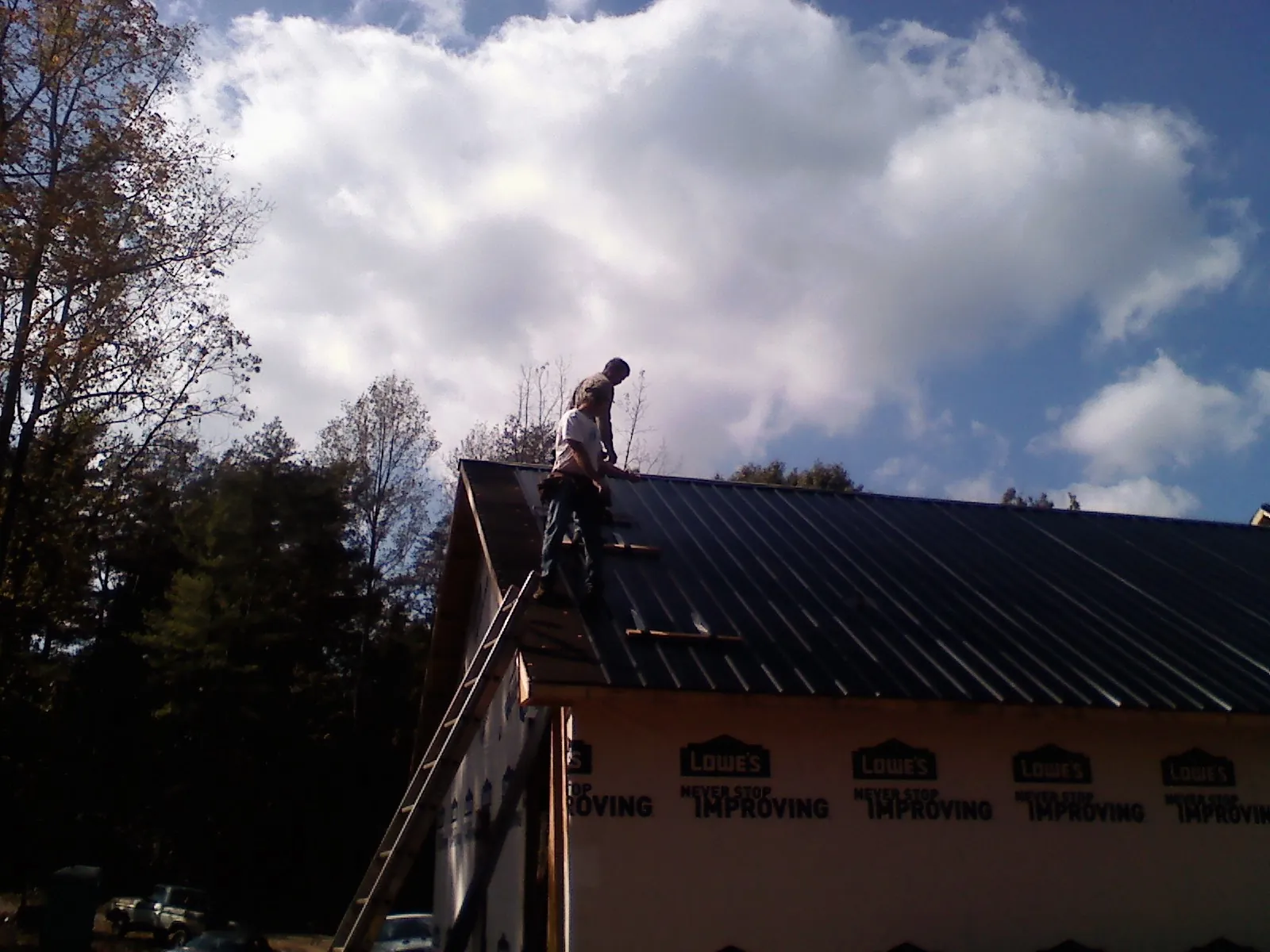 Roofer fastening dark metal panels high against a cloudy sky, from a Roof Inspection job in Boys Town