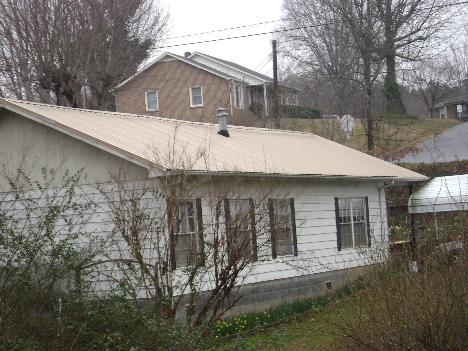 Tan metal roof on a white sided house set into a hillside — Commercial Roofing by Roofing Brothers in Boys Town