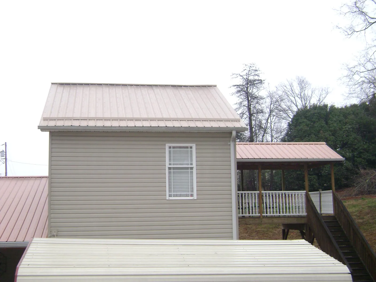Tan metal roofs on a two story addition and attached porch, from a Roof Replacement job in Boys Town